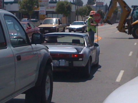 1968 Ford Mustang - A person directs traffic next to a silver sports car on a street with construction equipment visible.
