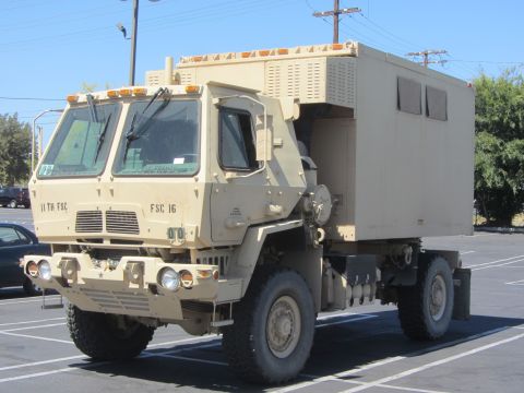 1968 Ford Mustang - A military truck with a large, box-like cargo compartment is parked in a lot under a bright sky.