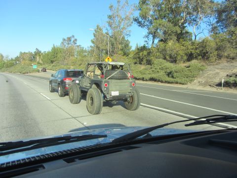 1968 Ford Mustang - A heavily modified Jeep-like vehicle tows a dark SUV on a sunny day on the highway.