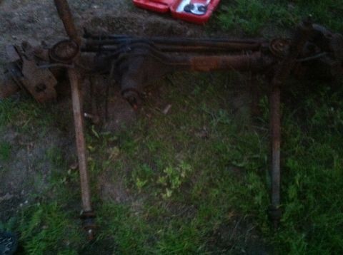 1989 Ford Bronco - A rusty vehicle axle assembly is shown lying on the grass, with a red toolbox in the background.