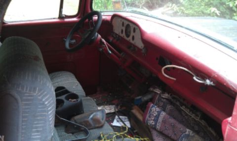 1957 Ford F-100 - The interior of a 1957 Ford F-100 shows a red dashboard, patterned seat, and a steering wheel.