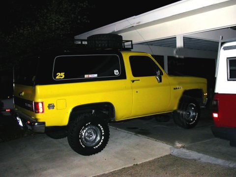 1981 Chevrolet Blazer - A yellow and black Chevrolet K5 Blazer is parked under a carport, with a spare tire mounted on its roof rack.