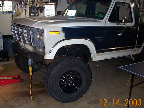 1986 Ford Bronco - Front view of a lifted 1980s Ford Bronco undergoing work in a garage setting.