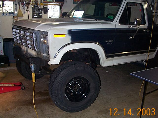 Two-tone lifted Ford truck on big tires and black wheels in a garage