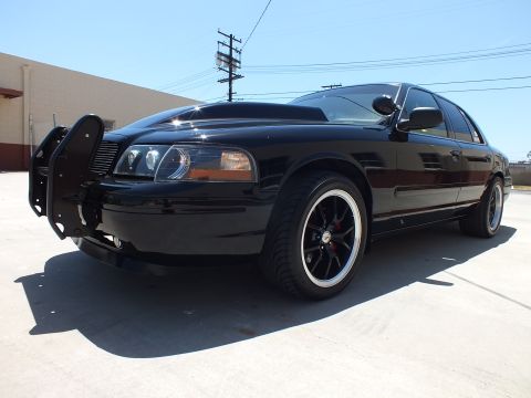 2003 Ford Crown Victoria - Close front-quarter view of a black Ford Crown Victoria fitted with a push bar and dark alloy wheels on white concrete.