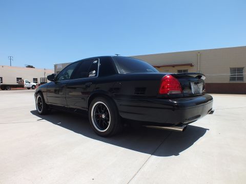 2003 Ford Crown Victoria - Rear-quarter view of a black Ford Crown Victoria with a trunk spoiler and dark wheels parked in a lot.