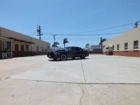 2003 Ford Crown Victoria - black sedan rests at distance in a large concrete lot with palm trees and tan buildings behind it.