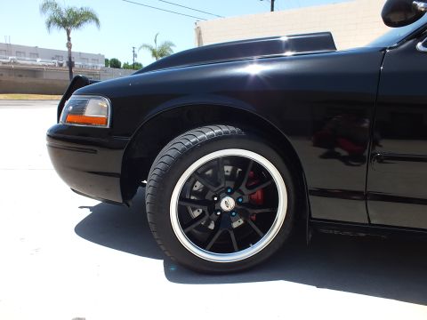 2003 Ford Crown Victoria - Detail of a black sedan's front fender and black multi-spoke alloy wheel with a red brake caliper.