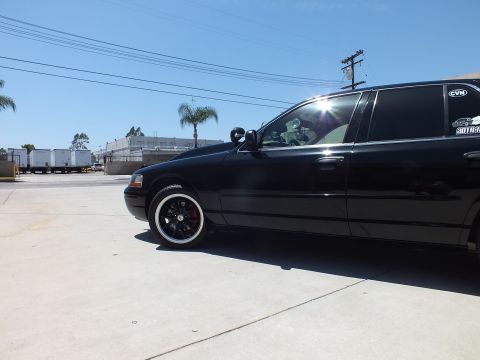 2003 Ford Crown Victoria - Low side-rear view of a black sedan with window decals and a black alloy wheel, sun flaring off the glass.