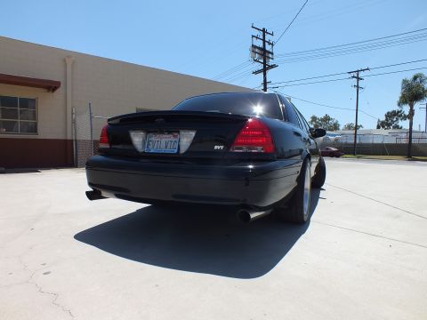 2003 Ford Crown Victoria - rear of a black Ford sedan shows an SVT badge and a California 'EVIL VTC' plate over a Crown Victoria frame.