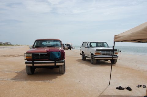 1994 Ford Bronco - Two 1994 Ford Broncos parked on a sandy beach with the ocean in the background.