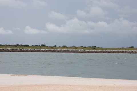 1994 Ford Bronco - A wide shot of a body of water with a sandy shore in the foreground and a distant lighthouse on a grassy embankment.