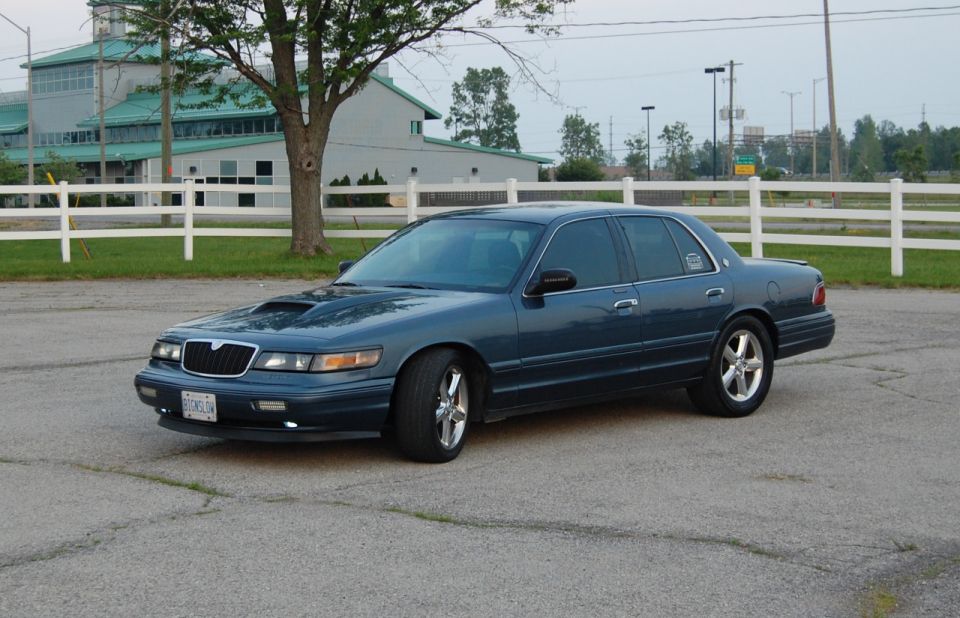 Dark blue Mercury Grand Marquis with a hood scoop parked outside
