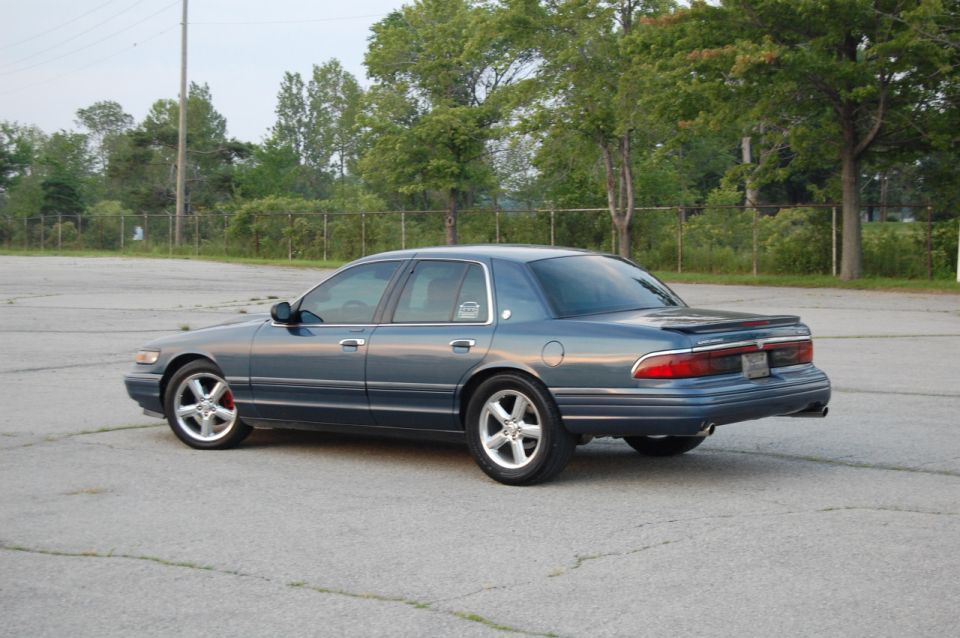 Blue sedan parked on asphalt lot, trees and fence in background