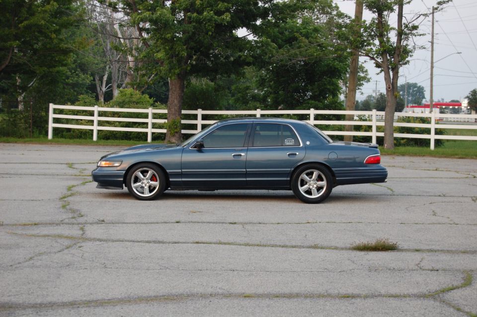 Blue Mercury Grand Marquis sedan parked on cracked asphalt, side view