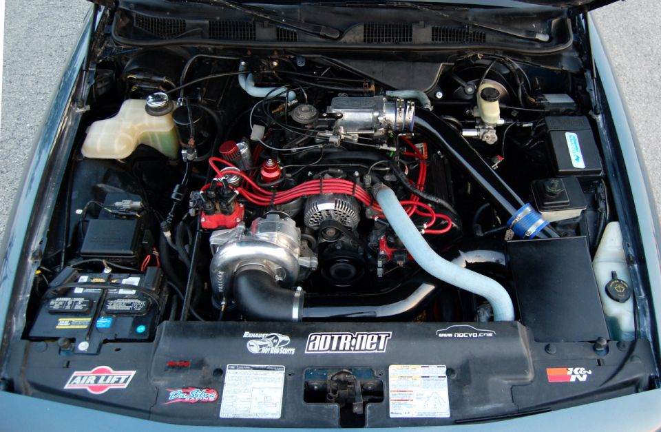 Engine bay with turbocharger, custom intake piping, and performance parts. Stickers for Air Lift, 20TR.net, K&N, and Supermotors.net are visible