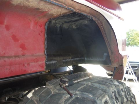 1968 Ford Bronco - Close-up of a red vehicle's rear wheel well undergoing modification, with a clamp securing the large tire.
