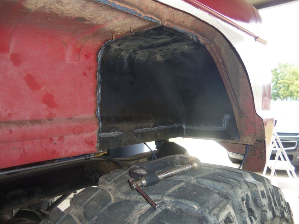 Red vehicle's rear wheel well being modified with a clamp on the tire