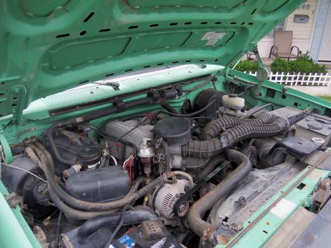 1968 Ford Bronco - The engine bay of a green vehicle is shown, various engine components and hoses.