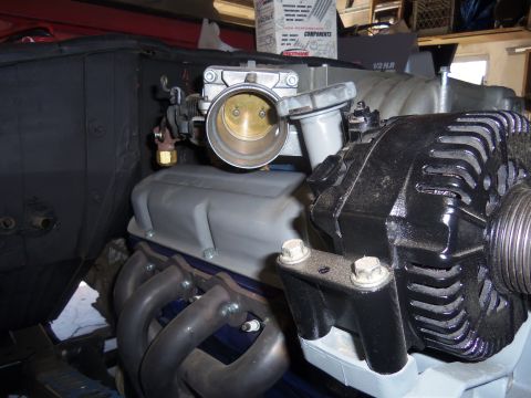 1968 Ford Bronco - Close-up view of engine parts, including an alternator, throttle body, and exhaust manifold, with visible text on a box in the background.