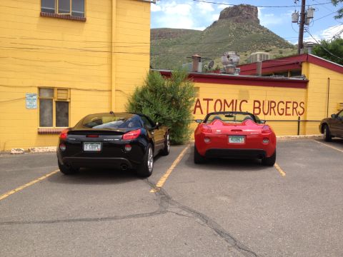 1995 Ford Bronco - Two Pontiac Solstice convertibles are parked in front of a yellow building with 'Atomic Burgers' painted on the side.