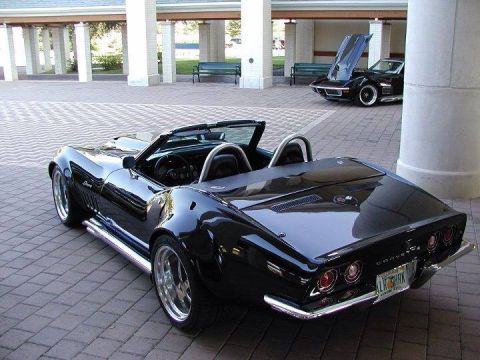 1976 Chevrolet Corvette - A black convertible Corvette is parked on a brick patio, with another Corvette in the background.