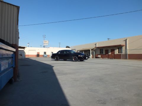2003 Ford Crown Victoria - distant black sedan is parked across an expansive industrial lot near a blue dumpster and warehouse buildings.