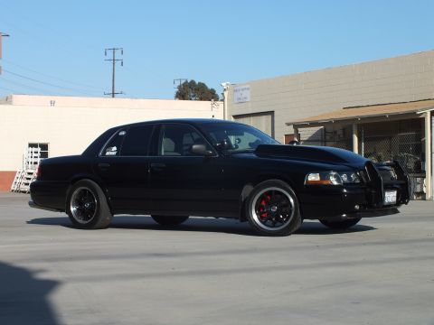 2003 Ford Crown Victoria - black full-size sedan poses in three-quarter front profile, showing chrome trim, black wheels, and red brake calipers.