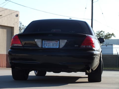 2003 Ford Crown Victoria - rear of a black Ford sedan shows an SVT badge, dual exhaust, and a California 'EVIL VTC' plate over a Crown Victoria frame.