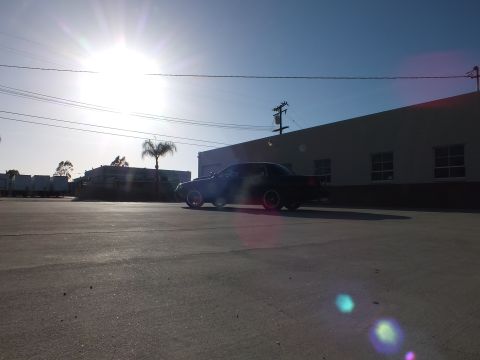 2003 Ford Crown Victoria - black sedan is silhouetted against intense backlighting and lens flare in an industrial parking lot.