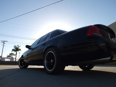 2003 Ford Crown Victoria - Low rear three-quarter view of a black sedan with red taillights, dark wheels and a small spoiler in a sunlit lot.