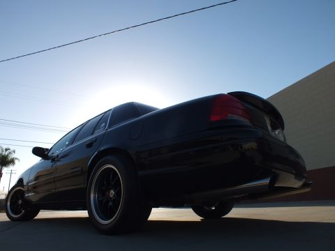2003 Ford Crown Victoria - black sedan shot from a low rear-quarter angle, highlighting its dark wheels, taillights and trunk-lip spoiler.