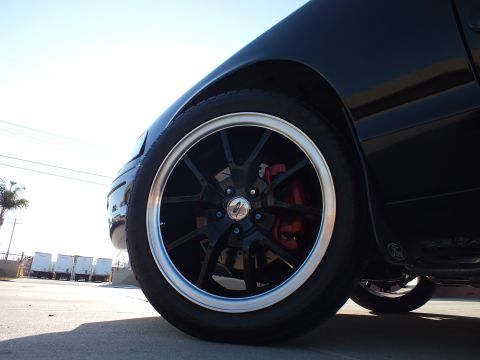 2003 Ford Crown Victoria - Low close-up of a black sedan's polished-lip black wheel and red brake caliper, with a Ford oval badge visible on the rear.