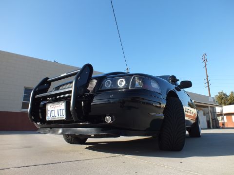 2003 Ford Crown Victoria - Low front view of a black sedan fitted with a police-style push bar, halo headlights and a California EVIL VIC plate.