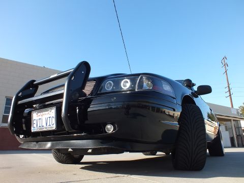 2003 Ford Crown Victoria - Low front angle of a black Ford Crown Victoria with a push bar, halo headlights and a California plate reading EVIL VIC.