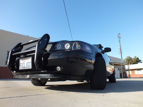 2003 Ford Crown Victoria - Low front-quarter view of a black sedan with a black push bar, halo headlights and a California EVIL VIC license plate.