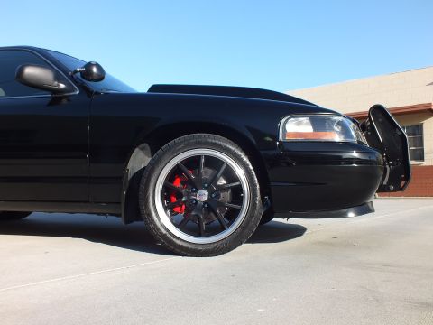 2003 Ford Crown Victoria - Front-quarter view of a black sedan with a black polished-lip wheel, red brake caliper and a front push bar.