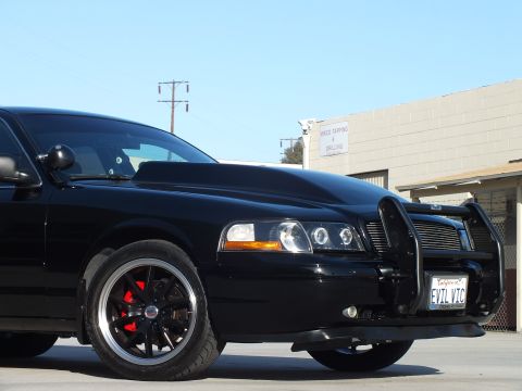 2003 Ford Crown Victoria - Close front-quarter detail of a black sedan showing its halo headlight, billet grille, push bar and EVIL VIC plate.