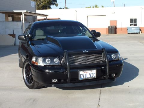 2003 Ford Crown Victoria - Head-on front view of a blacked-out full-size sedan with billet grille, push bar, halo headlights and an EVIL VIC plate.
