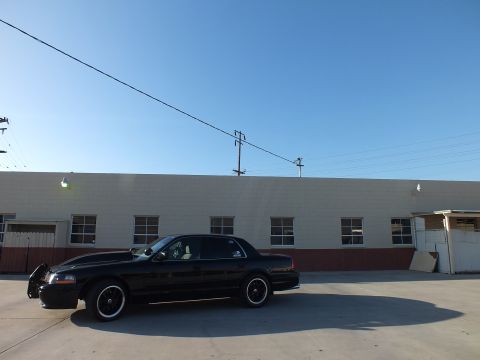 2003 Ford Crown Victoria - Side profile of a black Ford Crown Victoria with custom black-and-machined wheels parked in front of a warehouse.