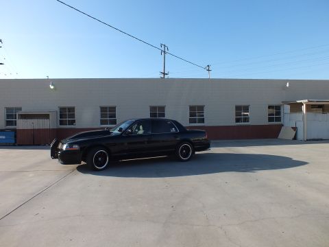 2003 Ford Crown Victoria - Side view of a lowered black Ford Crown Victoria sedan parked on concrete in front of a beige building.