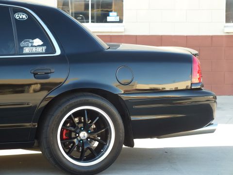 2003 Ford Crown Victoria - Close rear-quarter view of a black Crown Victoria showing a black-spoke wheel, red brake caliper, and window decals.