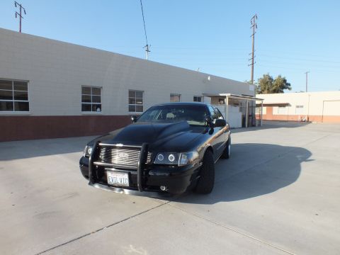 2003 Ford Crown Victoria - Front three-quarter view of a black Ford Crown Victoria with push bar parked in a sunlit industrial lot.