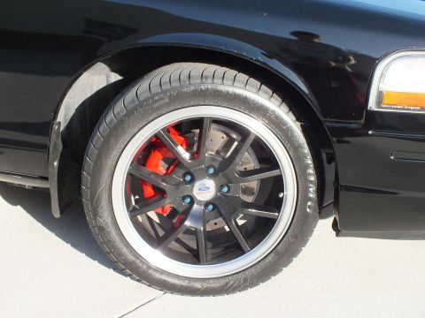 2003 Ford Crown Victoria - Close-up of a black multi-spoke wheel with a machined lip, red brake caliper, and Ford-branded center cap on a black car.