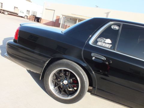 2003 Ford Crown Victoria - Rear-quarter view of a black Ford Crown Victoria with black wheels and window decals parked in an industrial lot.