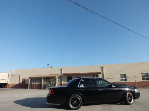 2003 Ford Crown Victoria - Side profile of a black Ford Crown Victoria parked on concrete in front of a long beige warehouse.