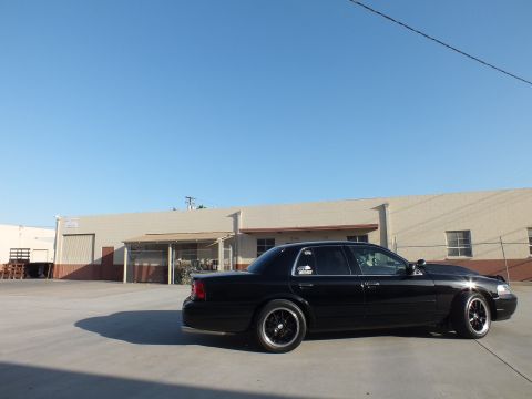 2003 Ford Crown Victoria - Side view of a black Ford Crown Victoria with black alloy wheels parked in a sunny industrial lot.