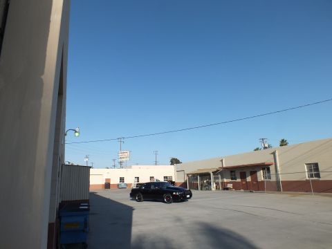 2003 Ford Crown Victoria - black sedan sits across a large concrete industrial lot, with warehouses and a sign under a clear blue sky.