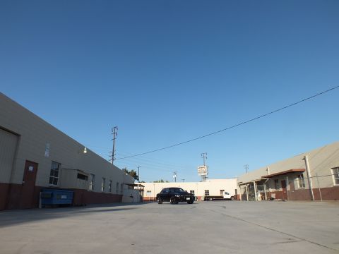 2003 Ford Crown Victoria - distant black sedan parked in a wide warehouse lot with a dumpster, utility poles, and a sign in the background.