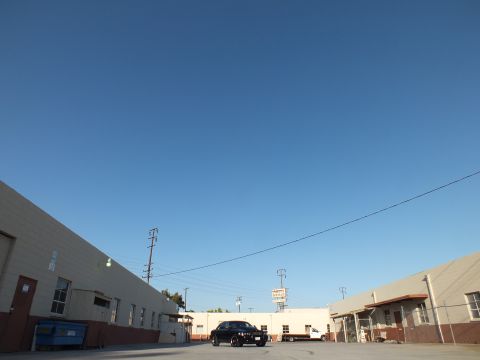 2003 Ford Crown Victoria - small black sedan parked in a large industrial lot beneath a wide expanse of clear blue sky.